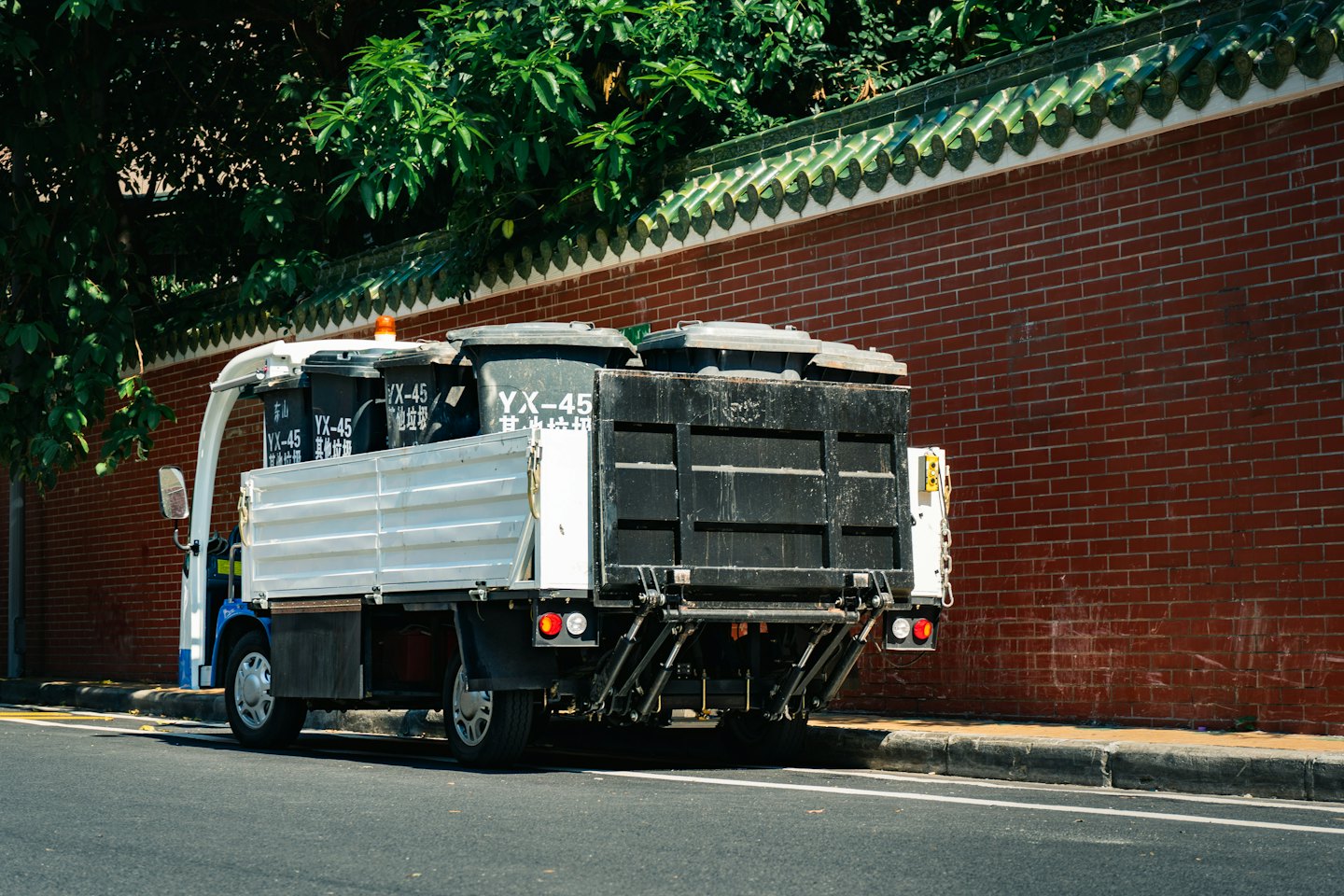 A utility truck loaded with garbage bins parked by a wall.