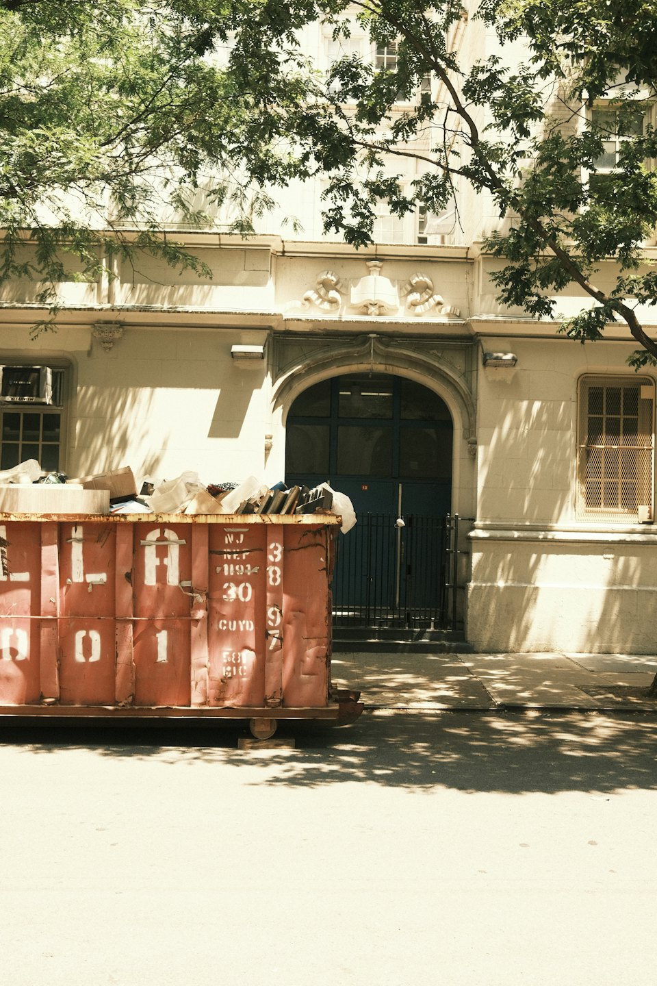 Rusted dumpster overflowing with construction debris outside an ornate building.