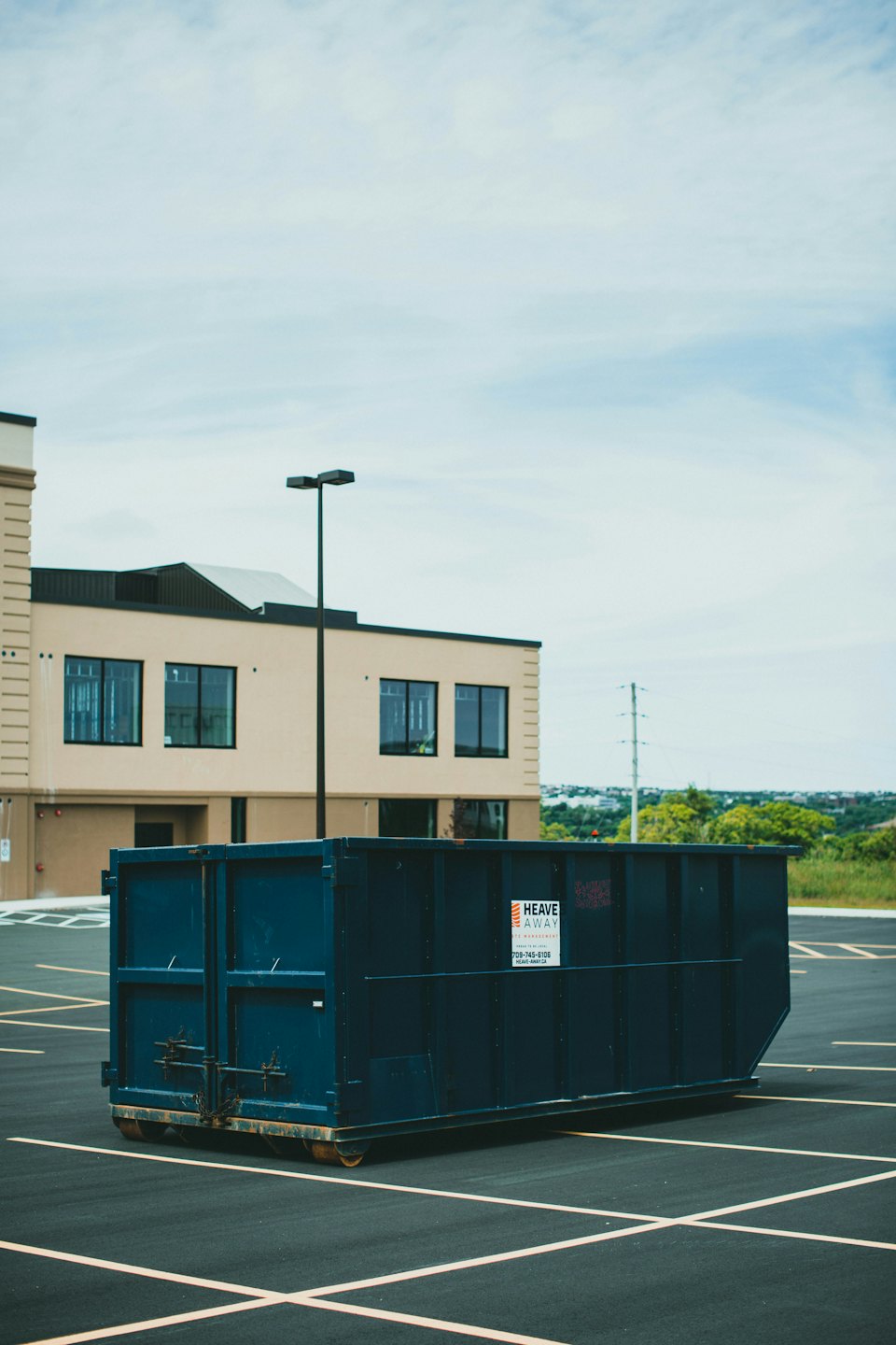 A large blue commercial dumpster sits in an asphalt parking lot.
